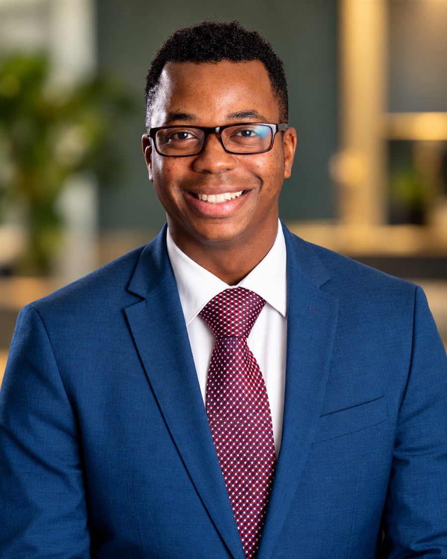 Jonathan Servance smiling in a blue suit in a warmly lit office.