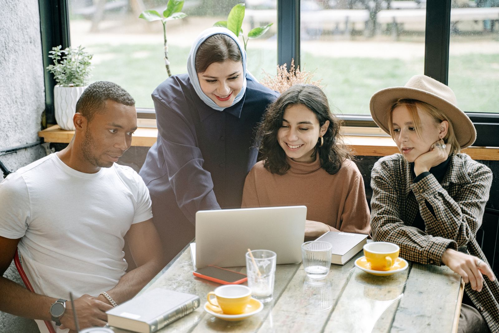 Four people from varied backgrounds collaborating around a laptop in a warm, naturally lit workspace.