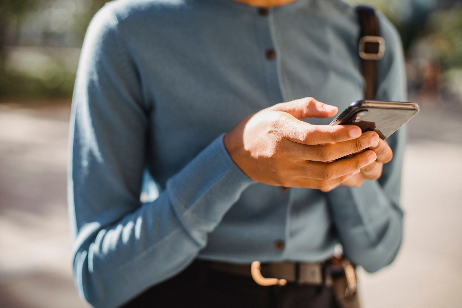 A person using a smartphone outdoors in warm natural light.